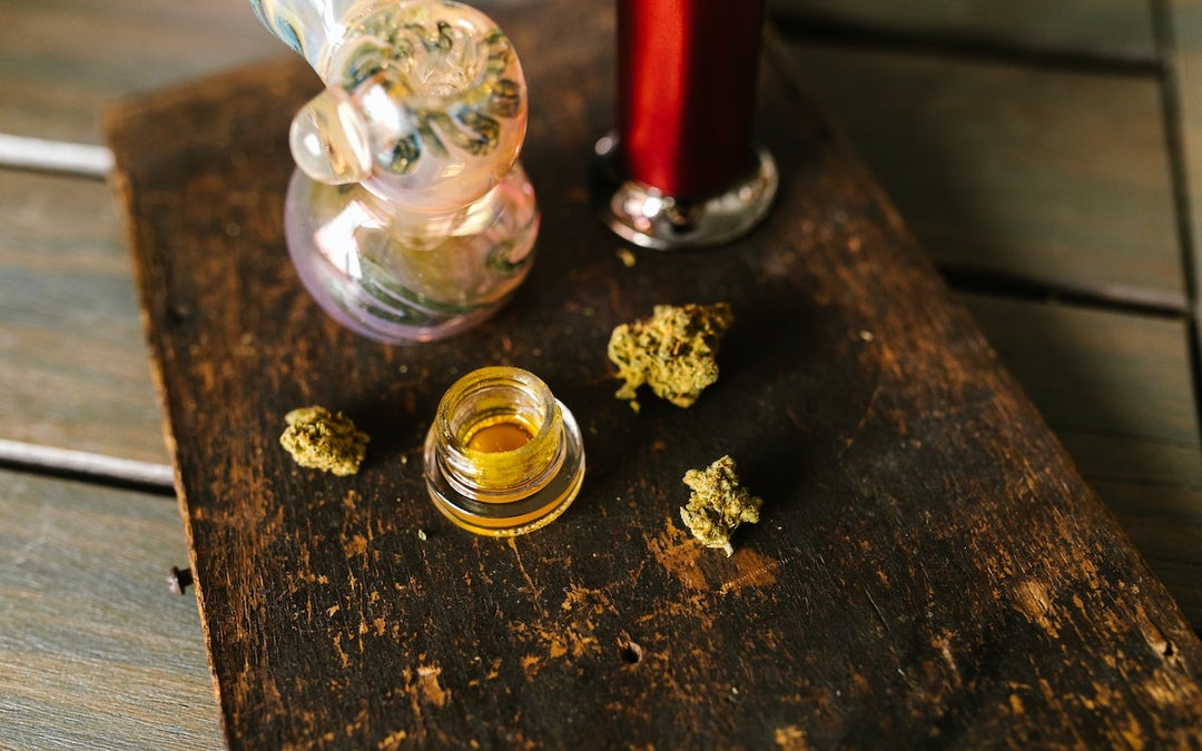 Various forms of cannabis placed on a brown table. There is a bong, flower and budder.