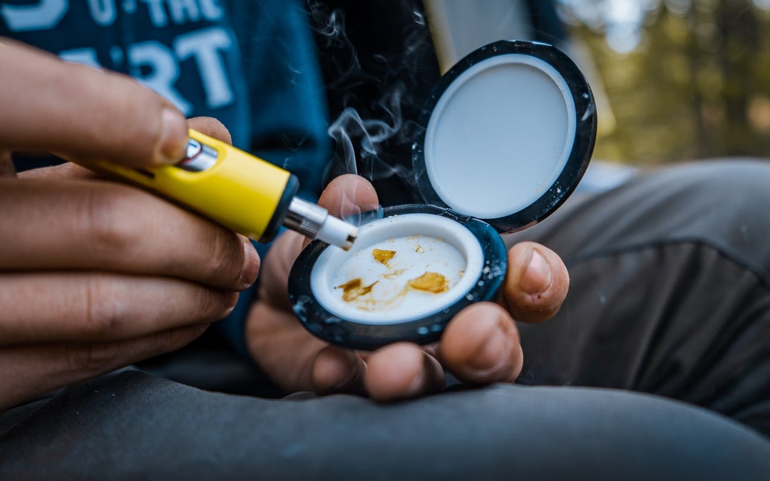 Young man heating up cannabis concentrates using a yellow dab pen.