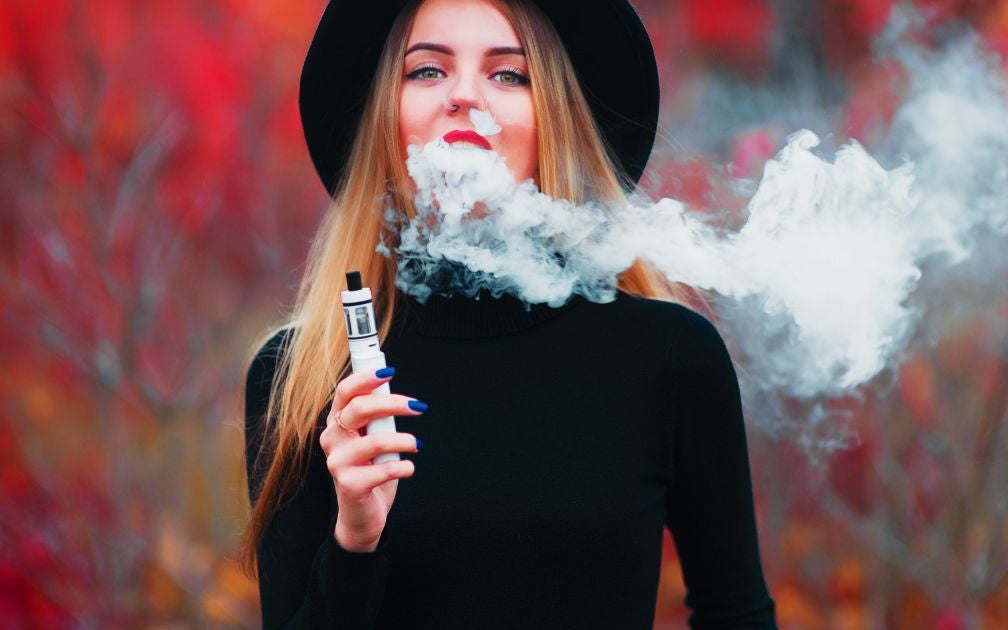 Young woman in black clothing and blonde hair is smoking a thc vape pen.