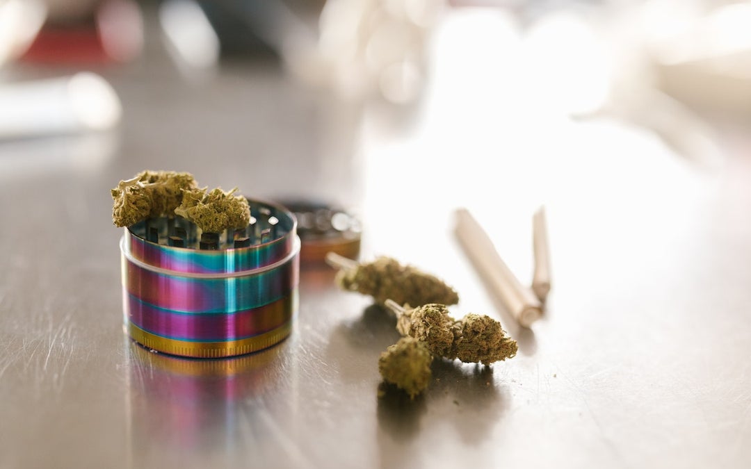 cannabis strain buds, two joints and a grinder sit on a metal table.