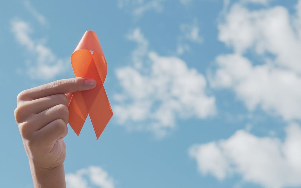 Ann orange ribbon that represents multiple sclerosis held up in front of the blue sky.