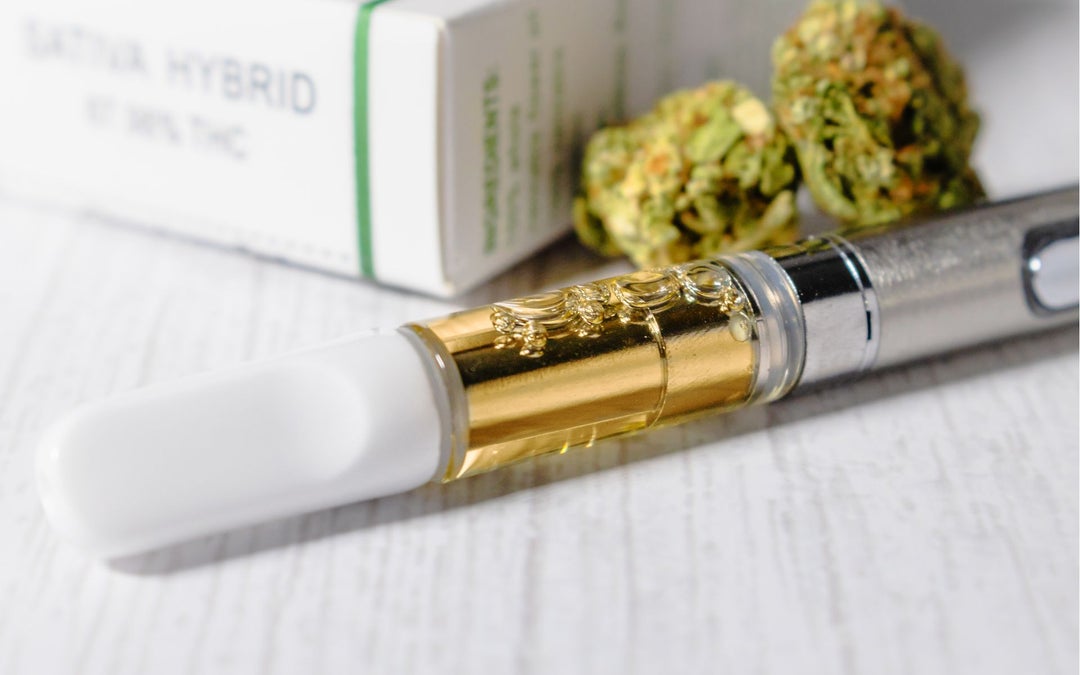 A white, gold and silver weed vape pen sits on a white wooden desk.